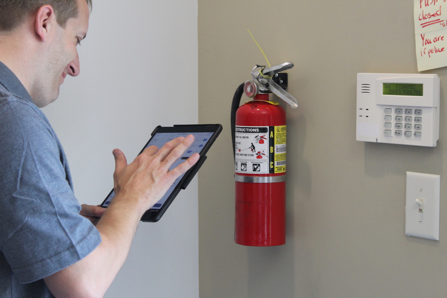 Man looking at Fire Inspection Software on Tablet, inspecting a fire extinguisher
